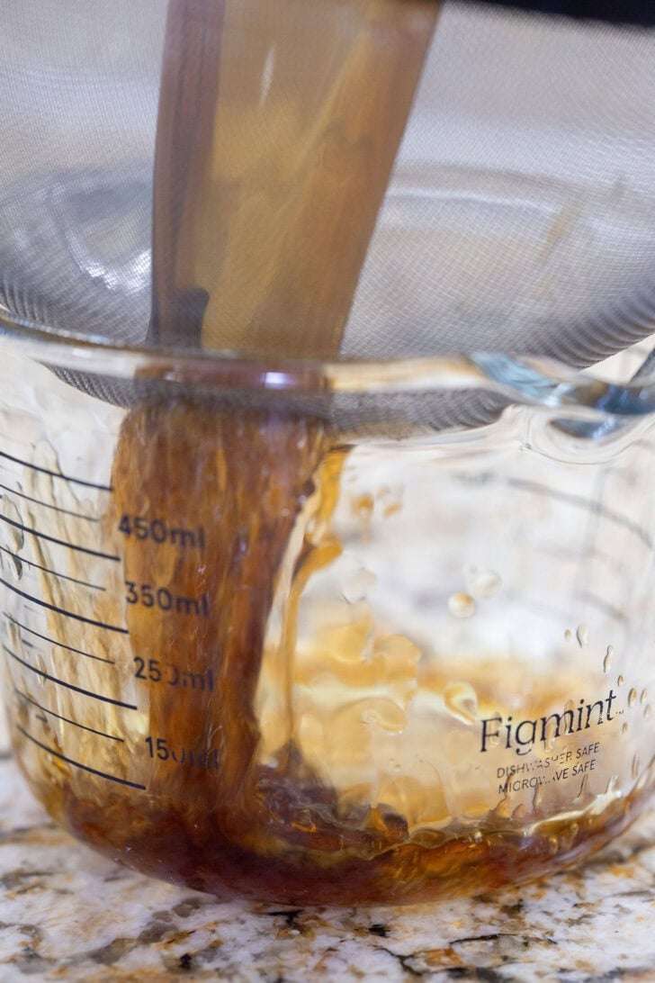 Straining gingerbread simple syrup through a fine-mesh sieve into a glass measuring cup.