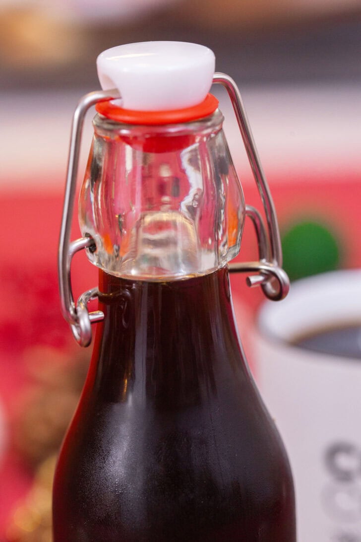 A very close-up shot of a sealed swing-top bottle of homemade gingerbread simple syrup on a festive red background.