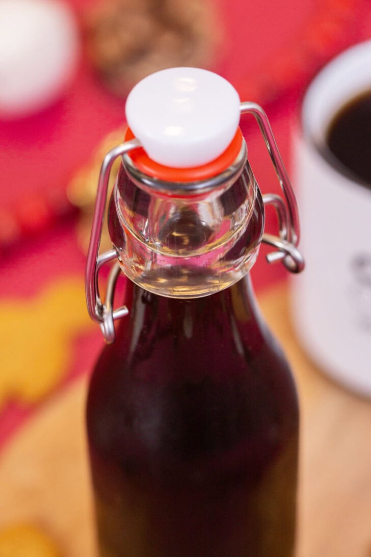 A close shot of the clear glass neck and swing-top lid of a bottle of dark gingerbread simple syrup.
