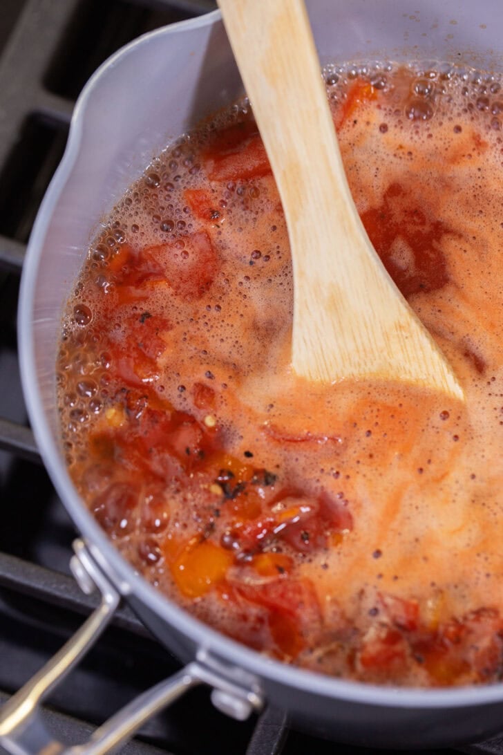 Crushed tomatoes, cannellini beans, and vegetable broth being mixed together in a pot to make 3-ingredient white bean tomato soup.