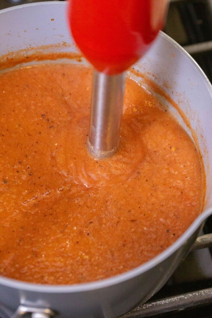Using an immersion blender to finish blending crushed tomatoes, cannellini beans, and vegetable broth into a smooth 3-ingredient white bean tomato soup.